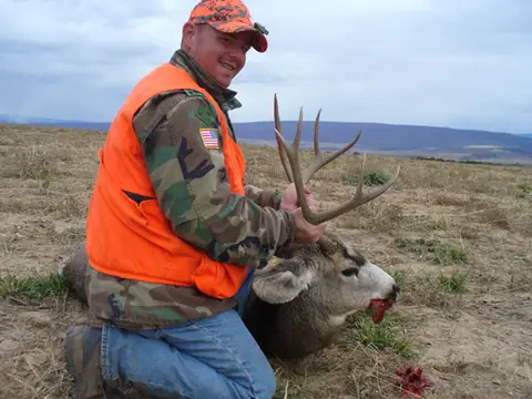 Hunter in blaze orange with a mule deer buck
